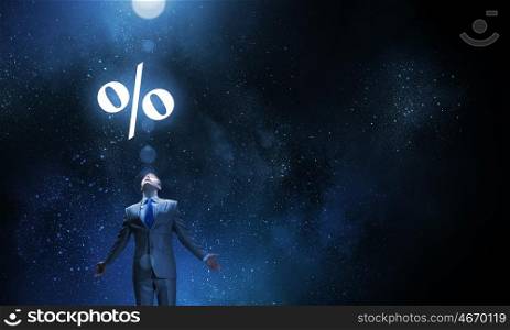 In light of success. Businessman with hands spread apart standing in light and percent sign above