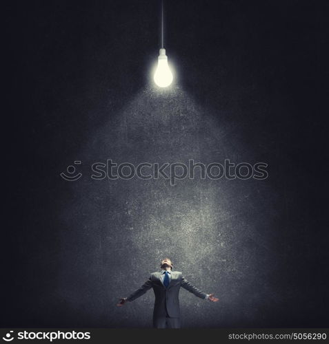 In light of success. Businessman with hands spread apart standing in light coming from above