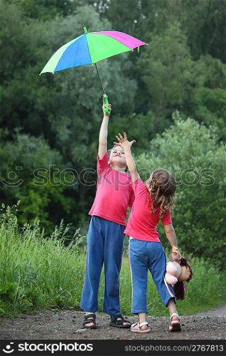In park boy holds umbrella over head, girl pulls to it hand