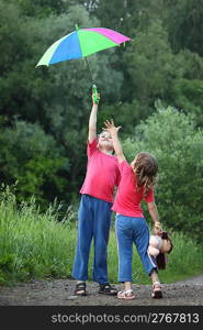 In park boy holds umbrella over head, girl pulls to it hand