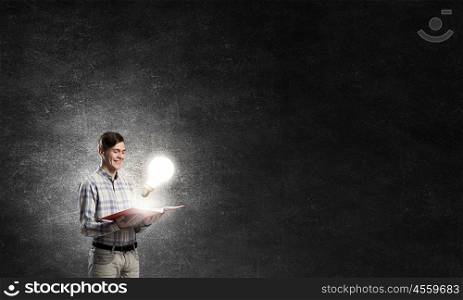 In search of bright inspiration. Young man holding opened book and glass glowing bulb on pages