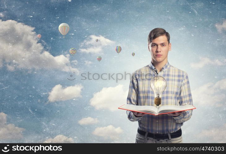 In search of bright inspiration. Young man holding opened book and glass glowing bulb on pages