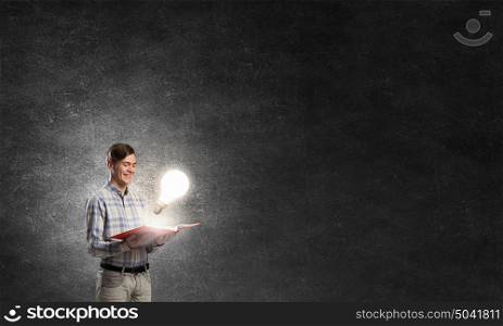 In search of bright inspiration. Young man holding opened book and glass glowing bulb on pages