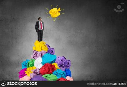 In search of good idea. Adult businessman standing on heap of paper balls