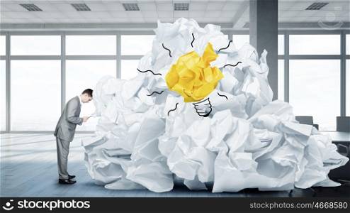 In search of good idea. Troubled businessman in office and heap of paper balls