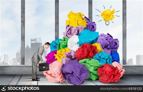 In search of good idea. Troubled businessman in office and heap of paper balls
