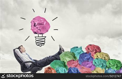 In search of great idea. Businessman in chair and many crumpled balls of colorful paper as creativity sign