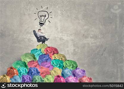In search of great idea. Businessman in chair and many crumpled balls of colorful paper as creativity sign