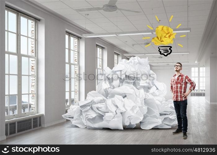 In search of his great idea. Young man in modern interior and paper balls as symbol of creativity