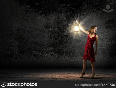 In search of something. Young attractive woman in red dress with lantern walking in darkness