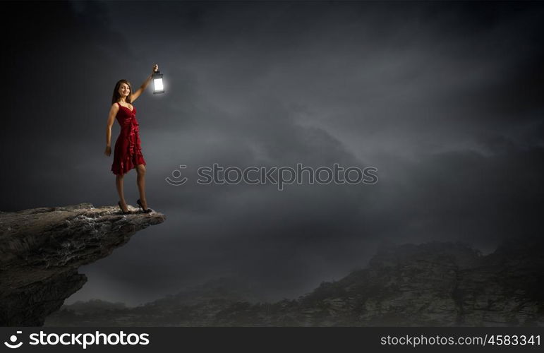 In search of something. Young attractive woman in red dress with lantern walking in darkness