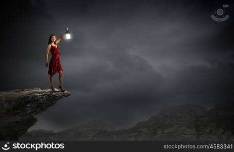 In search of something. Young attractive woman in red dress with lantern walking in darkness