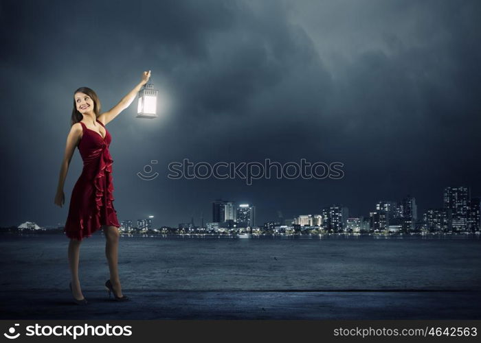 In search of something. Young attractive woman in red dress with lantern walking in darkness