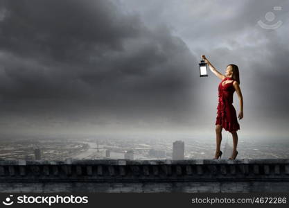 In search of something. Young attractive woman in red dress with lantern walking in darkness