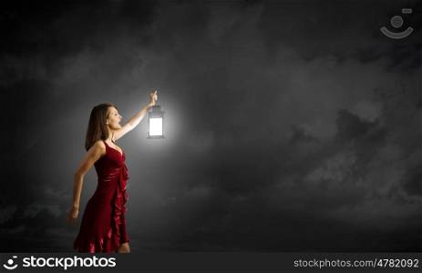 In search of something. Young attractive woman in red dress with lantern walking in darkness