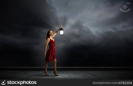 In search of something. Young attractive woman in red dress with lantern walking in darkness