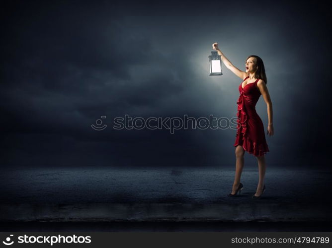 In search of something. Young attractive woman in red dress with lantern walking in darkness