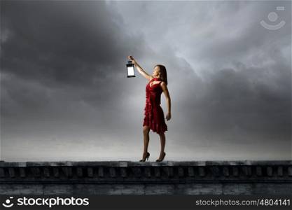 In search of something. Young attractive woman in red dress with lantern walking in darkness