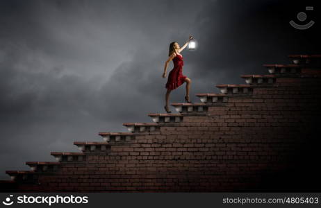 In search of something. Young attractive woman in red dress with lantern walking in darkness