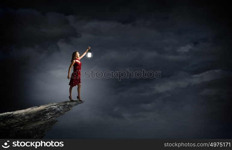 In search of something. Young attractive woman in red dress with lantern walking in darkness