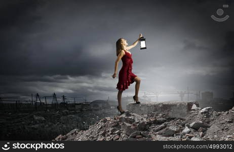 In search of something. Young attractive woman in red dress with lantern walking in darkness