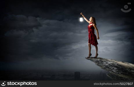 In search of something. Young attractive woman in red dress with lantern walking in darkness