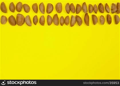 In shell raw almonds on yellow background with copy space