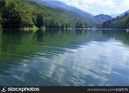In the clear waters of a mountain lake in the deciduous forest white clouds are reflected against the blue sky. Reflection of white clouds in the smooth surface of a forest mountain lake
