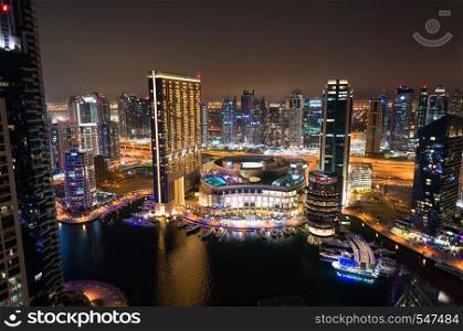 In the evening the city is full of life: cars driving on the road, the streets are glowing with is, people walk on sidewalks. Night view of Dubai city with roads, skyscrapers and bright lights