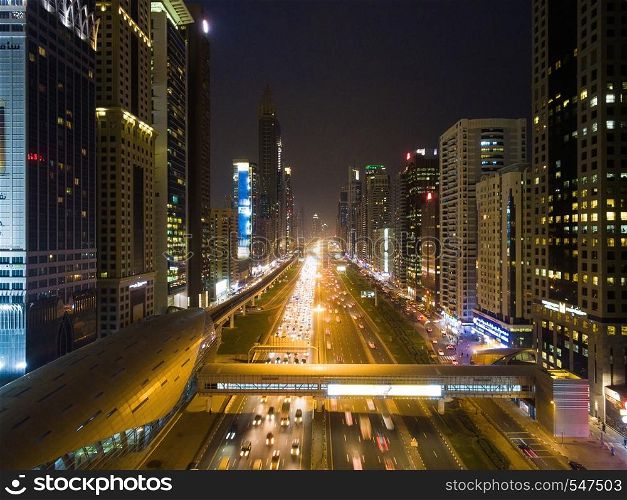 In the evening the city is full of life: cars driving on the road, the streets are glowing with is, people walk on sidewalks. Night view of Dubai city with roads, skyscrapers and bright lights
