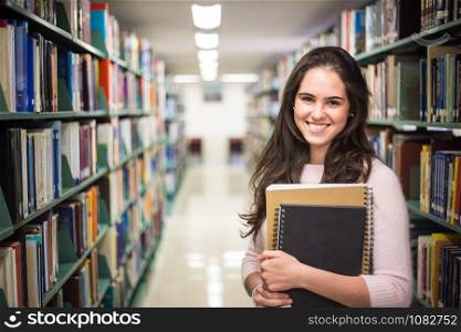 In the library - pretty female student with books working in a high school library.