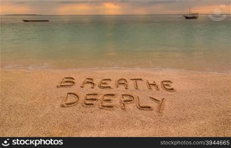 "In the photo a beach in Zanzibar at sunset where there is an inscription on the sand "Breathe Deeeply"."