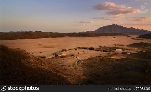 In the picture a beautiful view of a valley in the Egyptian desert at sunset a few kilometers from Marsa Alam, foreground a Bedouin village frequented by many tourists and background the rock mountains.