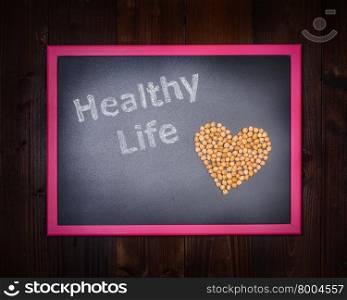"In the picture a blackboard, on the left side with written "Healthy Life" and chickpeas on the right side, drawing a heart on wooden background"