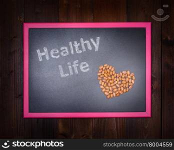"In the picture a blackboard, on the left side with written "Healthy Life" and on the right side of beans which draw a heart on wooden background"