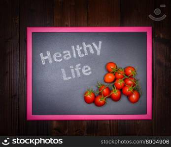 "In the picture a blackboard, on the left side with written "Healthy Life" and on the right side a cherry tomato on wooden background"
