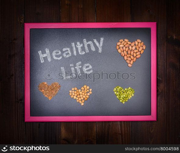 "In the picture a blackboard that says "Healthy Life" and around a set of hearts made from chickpeas, beans, lentils and peas on wooden background"