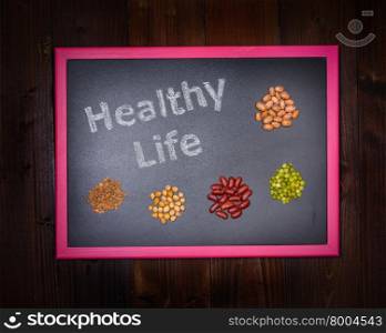"In the picture a blackboard that says "Healthy Life" and around small groups made up of chickpeas, beans, lentils and peas on wooden background"