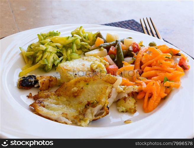 In the picture a fried fish fillet with vegetables served on white dish at the restaurant.