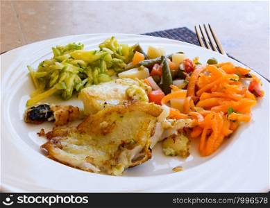 In the picture a fried fish fillet with vegetables served on white dish at the restaurant.