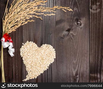 In the picture an ear of wheat and a heart formed by grains of rice on background of wood