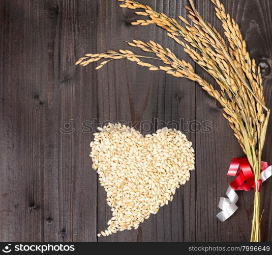 In the picture an ear of wheat and a heart formed by grains of rice on background of wood