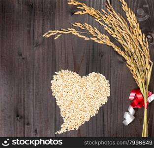 In the picture an ear of wheat and a heart formed by grains of rice on background of wood