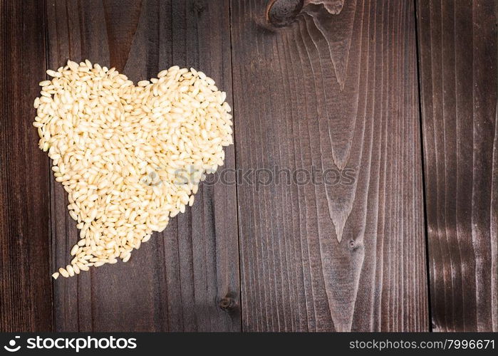 In the picture an heart formed by grains of rice on background of wood with empty space.