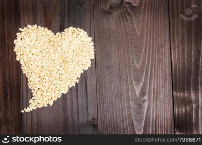 In the picture an heart formed by grains of rice on background of wood with empty space.