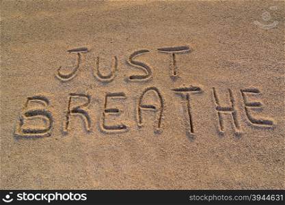 "In the picture the words on the sand "Just breathe"."