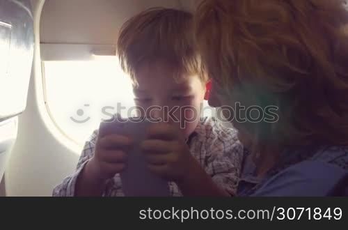 In the plane. Grandmother telling something to the grandchild while he using smartphone to entertain himself during the flight