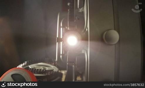 Includes two shots. Looking into the lens of an antique 8mm film projector as it is turned on and projecting beams of light. Includes projector audio.
