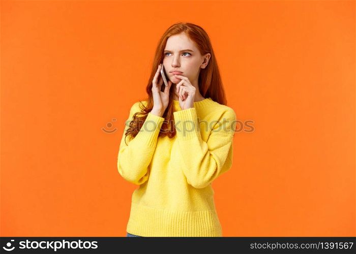 Indecisive and unsure, skeptical serious-looking redhead woman having tough decision make during conversation on phone, frowning touch lip pensive, order food delivery, orange background.. Indecisive and unsure, skeptical serious-looking redhead woman having tough decision make during conversation on phone, frowning touch lip pensive, order food delivery, orange background