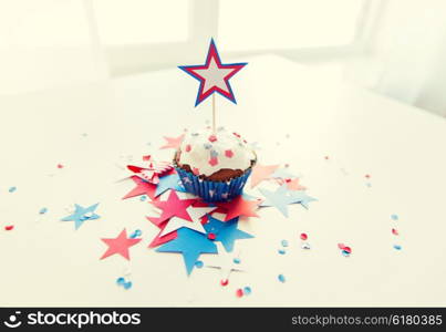 independence day, celebration, patriotism and holidays concept - close up of glazed cupcake or muffin decorated with star and cofetti on table at 4th july party